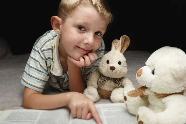 Bonito menino leitura livro com seus brinquedos favoritos — Fotografia de Stock