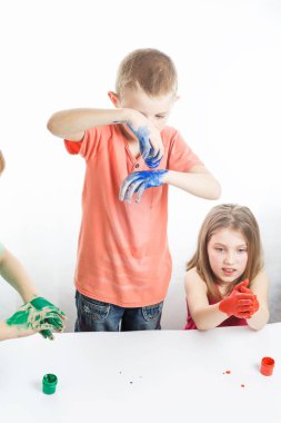 Çocuklar ellerini masaya koyup resim yaparlar.