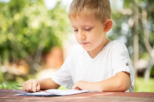 白いTシャツを着た小さな男の子が学校の概念に戻って屋外で読書しています. — ストック写真