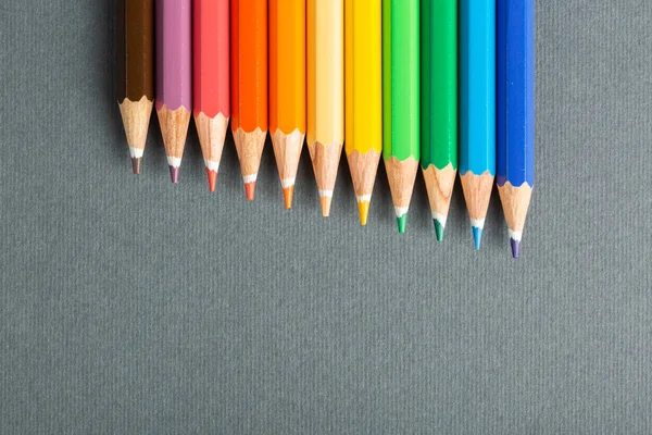 Colored pencils lined up in row on gray background — Stock Photo, Image