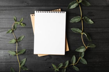 Yeşil yapraklı siyah tahta üzerine defter.