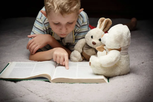 Kleine jongen lezen boek met zijn favoriete speelgoed — Stockfoto