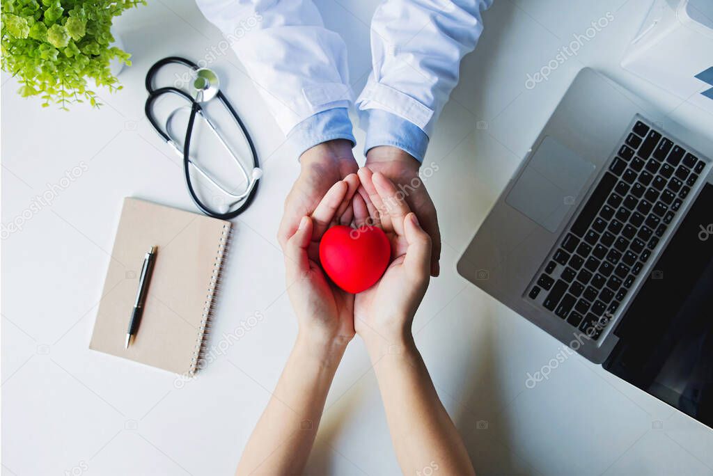 Top view . doctor and patient hands holding red heart on white table