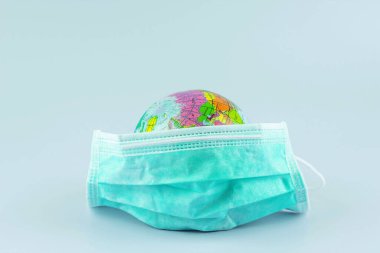 Mavi zemin üzerinde koruyucu yüz maskesi ve dünya modeli, yeni koronavirüs (2019-ncov) ve gribe karşı. Antiseptik, hijyen ve sağlık konsepti