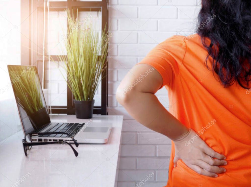 Young asian woman working with laptop computer and sitting on chair and suffering low spine back pain and waist sore, health concept and body aches.