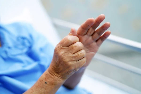 Asyalı yaşlı yaşlı kadın ya da yaşlı kadın hasta hemşire hastanede yatağında elini acıtıyor..