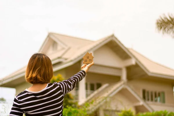 Small home model in woman hand front a home.