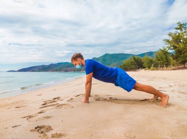 Coronavirus COVID 19. Spor yapan genç ve güzel bir adam sabah karantina sırasında denize yakın bir yerde egzersiz yapıyor. Yüz maskesi korumalı cerrahi sterilize yaşam