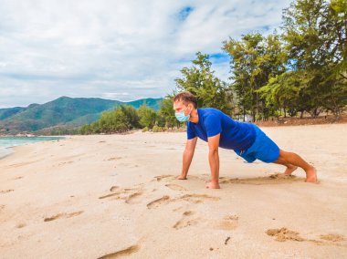 Coronavirus COVID 19. Spor yapan genç ve güzel bir adam sabah karantina sırasında denize yakın bir yerde egzersiz yapıyor. Yüz maskesi korumalı cerrahi sterilize yaşam