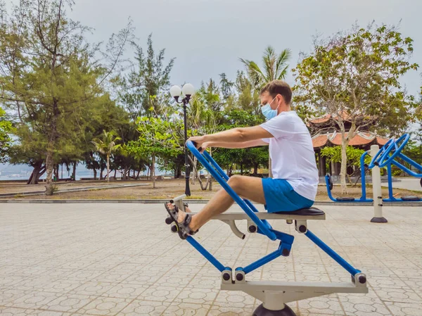 Man doing physical exercises, push ups, strength exercises, leans in empty outdoor public city park metal gym wearing mask alone for Covid19 prevention. Healthy lifestyle in quarantine and coronavirus