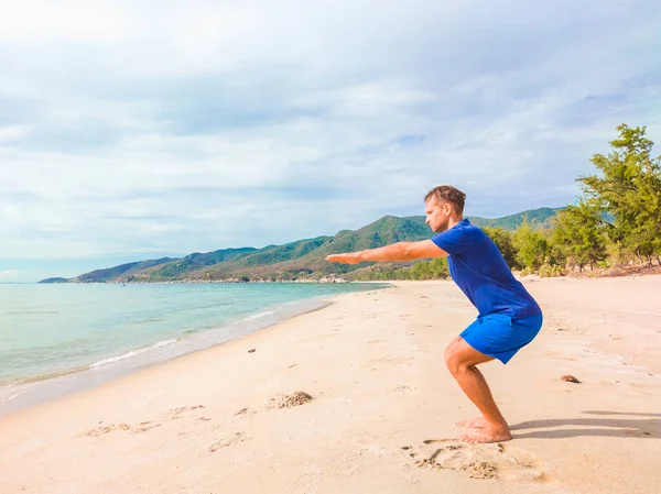 Pemuda tampan yang melakukan olahraga melakukan latihan latihan di dekat laut di pagi hari selama karantina. Kehidupan aktif tanpa operasi sterilisasi wajah perlindungan topeng — Stok Foto