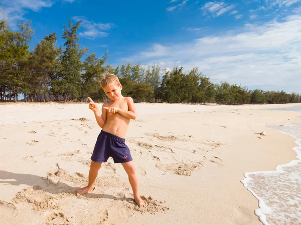 Micuţul băiat chipeş dansează pe plajă pe nisip curat sub cerul albastru, se bucură de vacanţă pe mare. Copilărie fericită și turism cu concept de copii — Fotografie, imagine de stoc