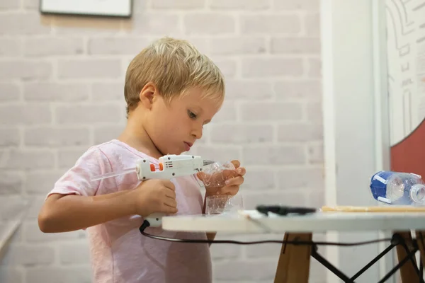 自己用回收的塑料瓶子做DIY玩具，用热熔胶枪做杯子。支持创意，手工制作。儿童在家居隔离时的创意休憩时间 — 图库照片
