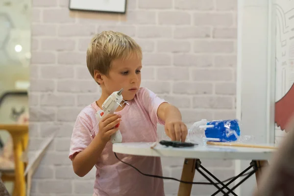 Tee se itse DIY leluja kierrätysmateriaaleista muovipullo, kuppi käyttäen kuumaliimaa ase. Luovuuden ja käsityön tukeminen. Luova vapaa-aika lapsille sisätiloissa karanteenin aikana koti shcool — kuvapankkivalokuva