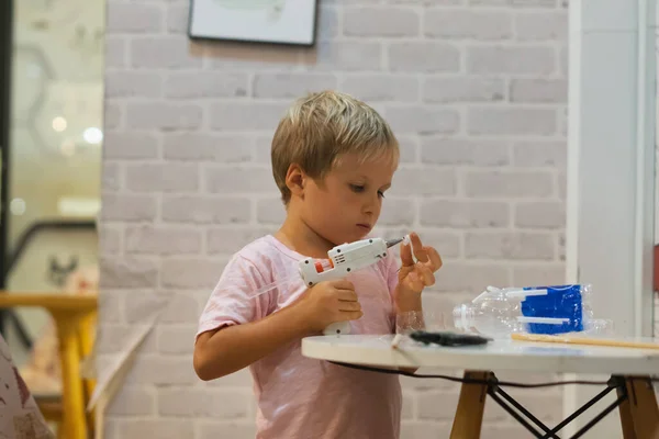 ทําด้วยตัวเองของเล่น DIY จากวัสดุรีไซเคิลขวดพลาสติกถ้วยโดยใช้ปืนกาวร้อนละลาย สนับสนุนความคิดสร้างสรรค์ งานฝีมือ การพักผ่อนที่สร้างสรรค์สําหรับเด็กในร่มในระหว่างการกักกันบ้านเย็น — ภาพถ่ายสต็อก