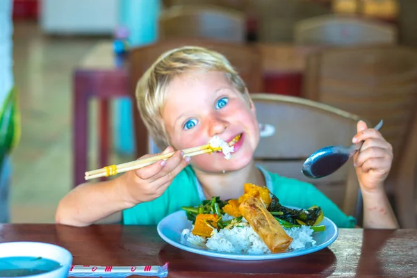 Zrób sobie przerwę. Wegetariańskie jedzenie może być pyszne dla każdego. Chłopiec jeść ryż i warzywa gulasz w białym talerzu z pałeczkami w prostej azjatyckiej kawiarni wegańskiej. Zdrowe odżywianie, dbanie o koncepcję zwierząt — Zdjęcie stockowe