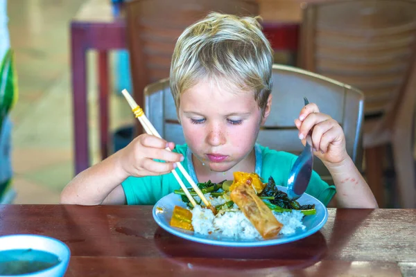 Beristirahatlah. Makanan vegetarian bisa lezat untuk semua orang. Anak laki-laki makan nasi dan sayuran rebus di piring putih dengan sumpit di kafe vegetarian Asia sederhana. Sehat makan, merawat konsep hewan — Stok Foto