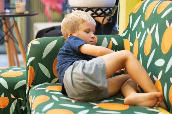 Egy ásító szomorú fiú unatkozik egyedül a kanapén. Önjáték otthon karantén alatt, vagy amíg a szülők elfoglaltak. A gyermekek oktatása, fejlesztése és a családi kapcsolatok fogalma — Stock Fotó