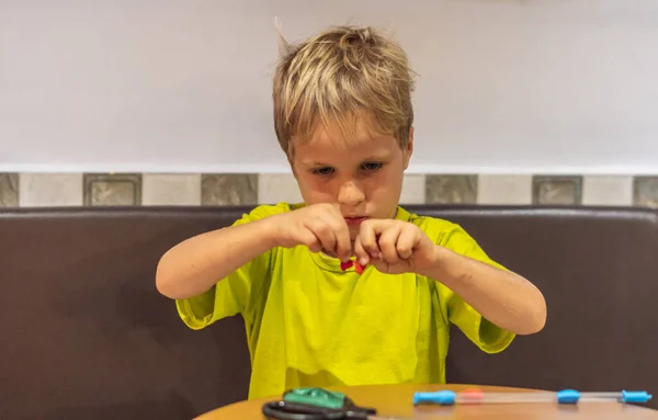 緑の黄色のTシャツの小さな男の子は、手作りの贈り物を作るオンライン学校の芸術や工芸品のクラスでリサイクル材料をカットします。子供の教育、開発コンセプト — ストック写真