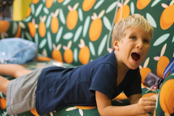 Χαριτωμένο θορυβώδες αγόρι ουρλιάζουν πολύ δυνατά σε ένα ξέσπασμα θυμού που βρίσκεται στον καναπέ. Εκπαίδευση, ανάπτυξη και οικογενειακή σχέση των παιδιών έννοια — Φωτογραφία Αρχείου