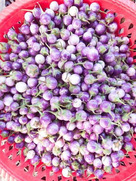 Gros plan tas de pile colorée de petites aubergines fraîches violettes naines crues sur un marché fermier asiatique local. Fond violet clair. Concept de cuisine et d'aliments sains, vitamines pour une immunité forte — Photo