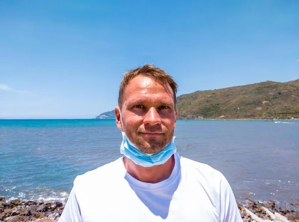 Portrait of a guy with a medical mask. Happy Man take off protective medical face used masks symbol the end of quarantine Covid 19 isolation and beginning of normal life again. Near blue sea and sky