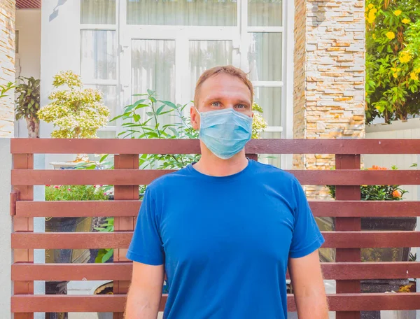 Portrait of guy with a medical mask. Outside walking in the garden near modern summer house. He wants to breathe, wait for the end of quarantine Covid19 isolation and beginning of normal life again