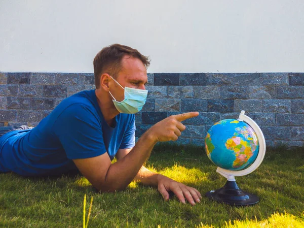Pria mengenakan masker wajah memegang peta dunia bumi di tangan. Karantina dirimu untuk melindungi penyebaran virus. Kapan bisa bepergian lagi. Pandemi epidemi coronavirus 2019-ncov sars covid-19 konsep virus — Stok Foto