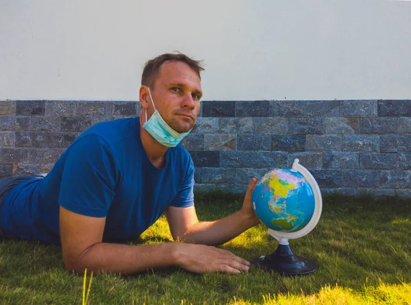 Man wearing Face Mask holding the Earth globe world map in hand. Quarantine yourself to protect spread virus. When can travel again. Epidemic pandemic coronavirus 2019-ncov sars covid-19 virus concept