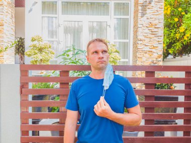 Tıbbi maskeli bir adamın portresi. Dışarıda, modern yazlığın yakınındaki bahçede yürüyorum. Nefes almak istiyor, karantinanın bitmesini bekliyor. Karantina 19 izolasyon ve normal hayatın yeniden başlamasını bekliyor.
