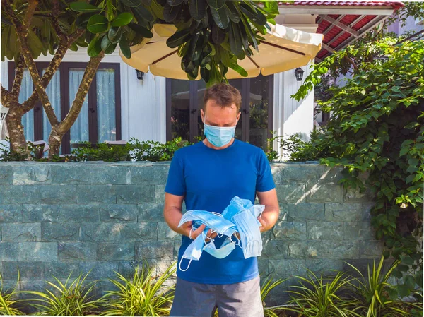 Guy with medical mask. Outside walking in the garden near modern summer house, wants to breathe, throw away mask, wait for the end of quarantine Covid 19 isolation and beginning of normal life again