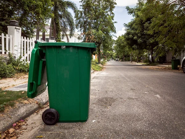 Membuka tempat sampah plastik hijau kosong besar di depan rumah modern dengan pohon hijau. Tidak ada sampah publik di pinggir jalan. Pengendalian infeksi, pembuangan sampah, pembuangan konsep limbah Stok Gambar Bebas Royalti