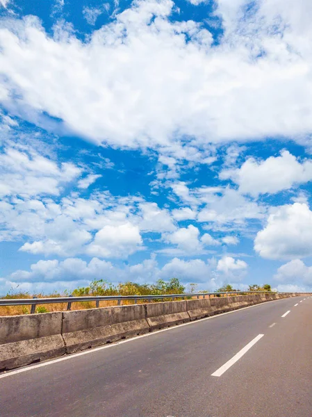 Suchý asfalt prázdný automobil rovná silnice s betonovou bariérou a značící čáry za slunečného letního dne s modrou oblačnou oblohou. Cestování autem koncepce pozadí. Svislý formát příběhů — Stock fotografie