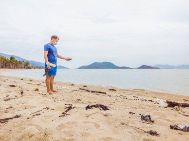 Eldivenli adam denizi kirleten plastik torbalar alıyor. İnsan kaynaklı kirliliğin yol açtığı kumsala çöp dökme sorunu, konsept olarak gönüllü temizleme kampanyası