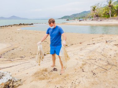 Eldivenli adam denizi kirleten plastik torbalar alıyor. İnsan yapımı kirlilik ve çevresel kirliliğin yol açtığı kumsala çöp dökme sorunu, konsept olarak gönüllü temizleme kampanyası