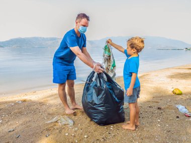Genç mutlu aile eylemcileri plajda plastik atık topluyor. Baba ve oğul gönüllü olarak çöpleri temizliyor. Çevre kirliliği sorunları. Açık hava yaşam tarzı eğlencesi. Çocukların doğal eğitimi