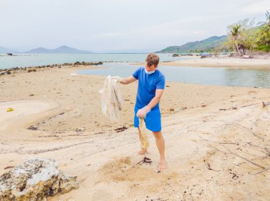 Eldivenli adam denizi kirleten plastik torbalar alıyor. İnsan kaynaklı kirliliğin yol açtığı kumsala çöp dökme sorunu, konsept olarak gönüllü temizleme kampanyası