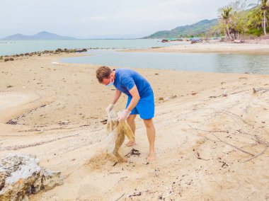Eldivenli adam denizi kirleten plastik torbalar alıyor. İnsan yapımı kirlilik ve çevresel kirliliğin yol açtığı kumsala çöp dökme sorunu, konsept olarak gönüllü temizleme kampanyası