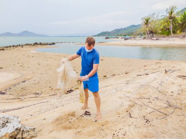 Eldivenli adam denizi kirleten plastik torbalar alıyor. İnsan yapımı kirlilik ve çevresel kirliliğin yol açtığı kumsala çöp dökme sorunu, konsept olarak gönüllü temizleme kampanyası