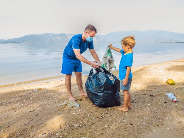 Aktivis keluarga muda yang bahagia mengumpulkan sampah plastik di pantai. Ayah dan anak sukarela membersihkan sampah. Masalah polusi lingkungan. Rekreasi gaya hidup luar ruangan. Pendidikan alami anak-anak — Stok Foto
