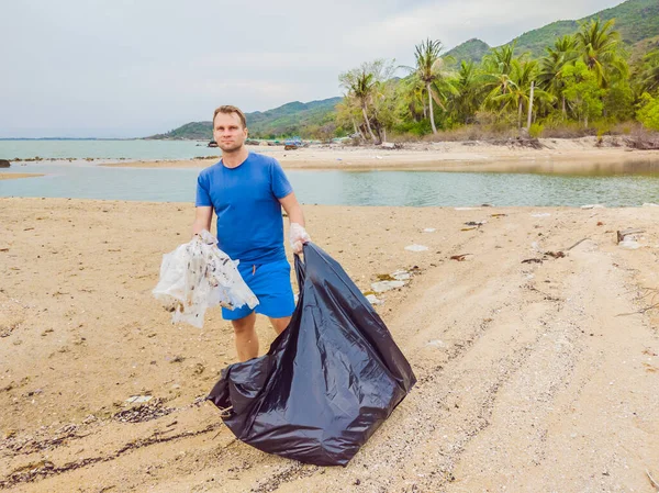 Manusia dalam sarung tangan mengambil kantong plastik yang mencemari laut. Masalah tumpah sampah sampah di pasir pantai disebabkan oleh polusi buatan manusia dan lingkungan, kampanye untuk membersihkan diri secara sukarela dalam konsep — Stok Foto