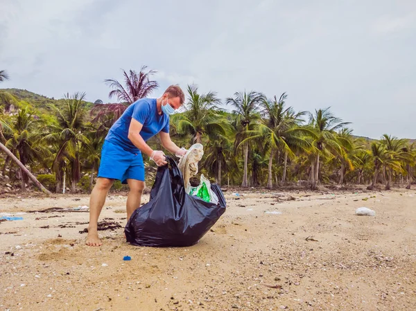 Man in gloves pick up plastic bags that pollute sea. Problem of spilled rubbish trash garbage on the beach sand caused by man-made pollution, campaign to clean volunteer in concept