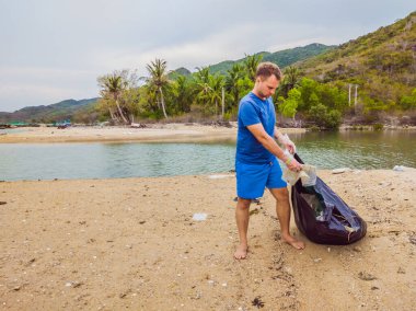 Eldivenli adam denizi kirleten plastik torbalar alıyor. İnsan yapımı kirlilik ve çevresel kirliliğin yol açtığı kumsala çöp dökme sorunu, konsept olarak gönüllü temizleme kampanyası