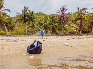 Eldivenli adam denizi kirleten plastik torbalar alıyor. İnsan kaynaklı kirliliğin yol açtığı kumsala çöp dökme sorunu, konsept olarak gönüllü temizleme kampanyası