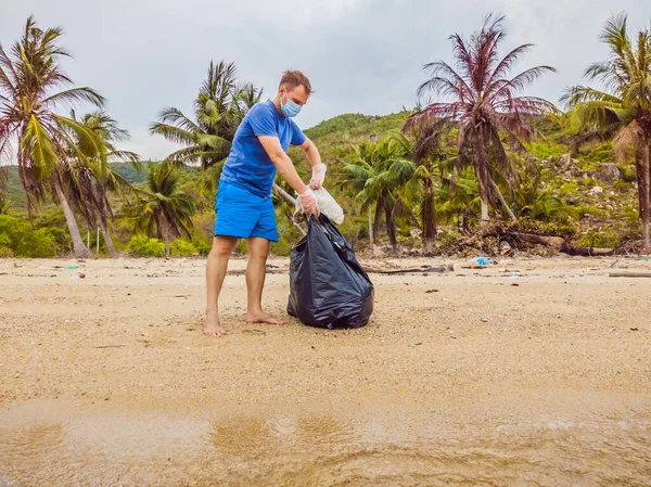 Man in gloves pick up plastic bags that pollute sea. Problem of spilled rubbish trash garbage on the beach sand caused by man-made pollution, campaign to clean volunteer in concept