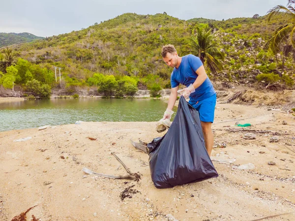 Eldivenli adam denizi kirleten plastik torbalar alıyor. İnsan yapımı kirlilik ve çevresel kirliliğin yol açtığı kumsala çöp dökme sorunu, konsept olarak gönüllü temizleme kampanyası