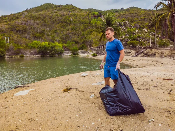 Manusia dalam sarung tangan mengambil kantong plastik yang mencemari laut. Masalah tumpah sampah sampah di pasir pantai disebabkan oleh polusi buatan manusia dan lingkungan, kampanye untuk membersihkan diri secara sukarela dalam konsep — Stok Foto