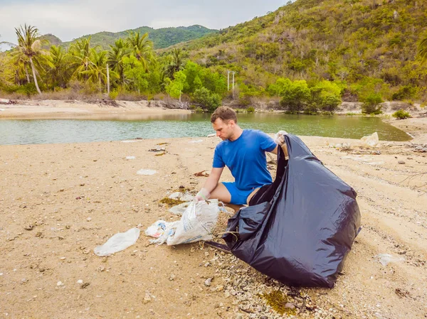 Man in gloves pick up plastic bags that pollute sea. Problem of spilled rubbish trash garbage on the beach sand caused by man-made pollution and environmental, campaign to clean volunteer in concept