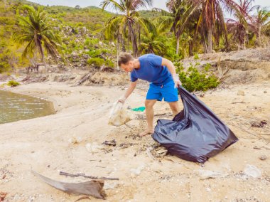Eldivenli adam denizi kirleten plastik torbalar alıyor. İnsan yapımı kirlilik ve çevresel kirliliğin yol açtığı kumsala çöp dökme sorunu, konsept olarak gönüllü temizleme kampanyası