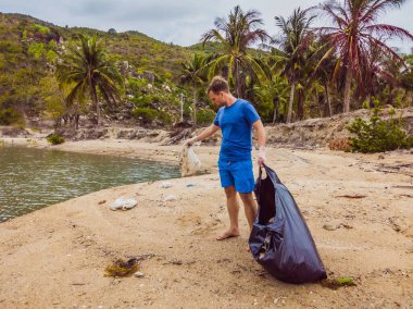 Eldivenli adam denizi kirleten plastik torbalar alıyor. İnsan yapımı kirlilik ve çevresel kirliliğin yol açtığı kumsala çöp dökme sorunu, konsept olarak gönüllü temizleme kampanyası